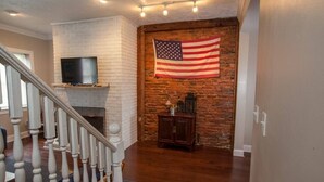 Een woonkamer met een haard van baksteen, een Amerikaanse vlag en een trap met witte spijlen.