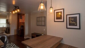 Een eetruimte met een houten tafel, hangende hanglampen en afbeeldingen in lijsten aan de muur.