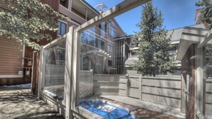 Ett område med ett bubbelbad, omgivet av glasväggar, ett trädäck och utsikt över en bostadsbyggnad.