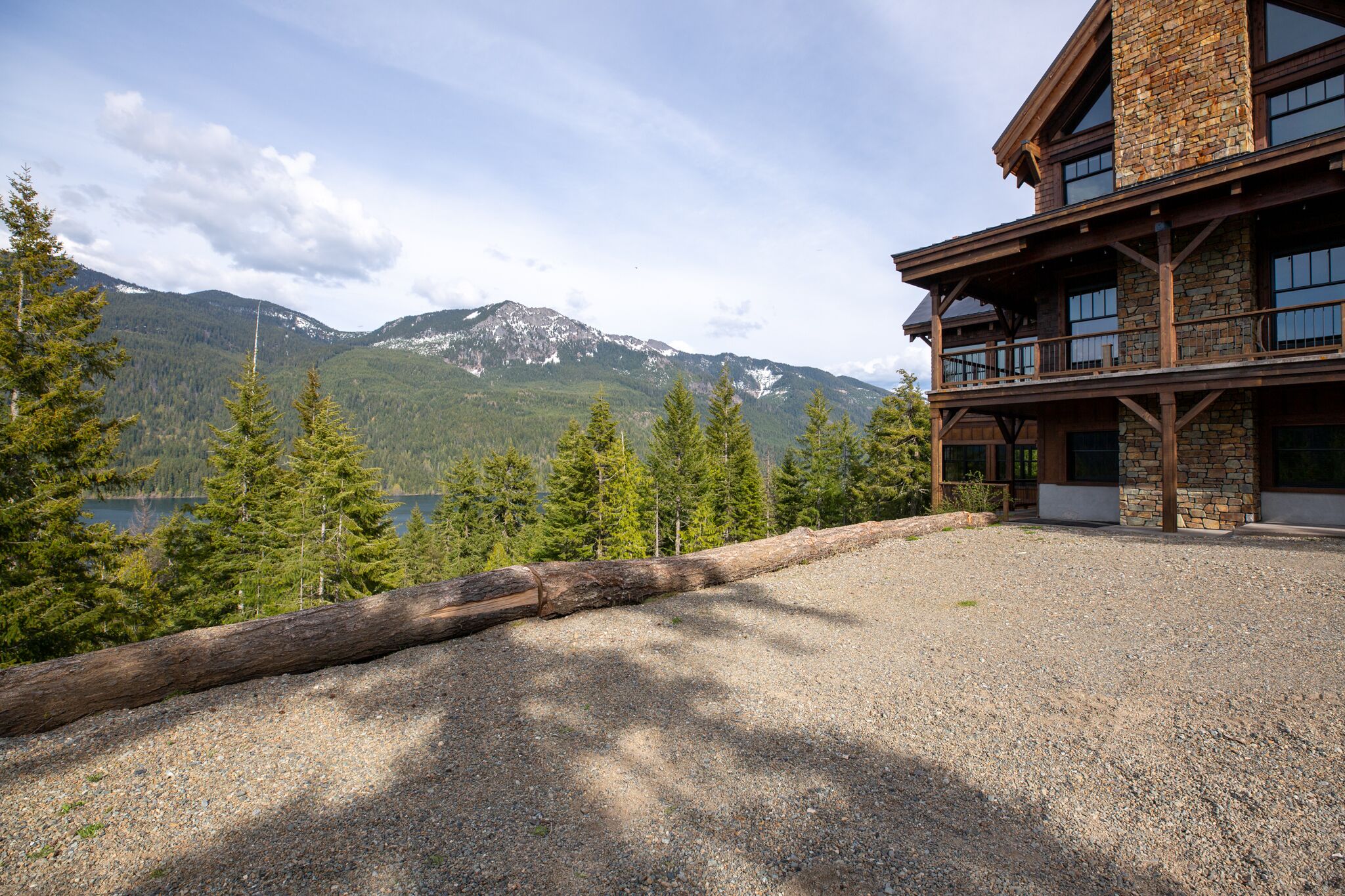 A lodge with a stone facade, large windows, and a view of mountains and a lake.