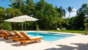 A pool area with lounge chairs and a large umbrella, surrounded by lush greenery.