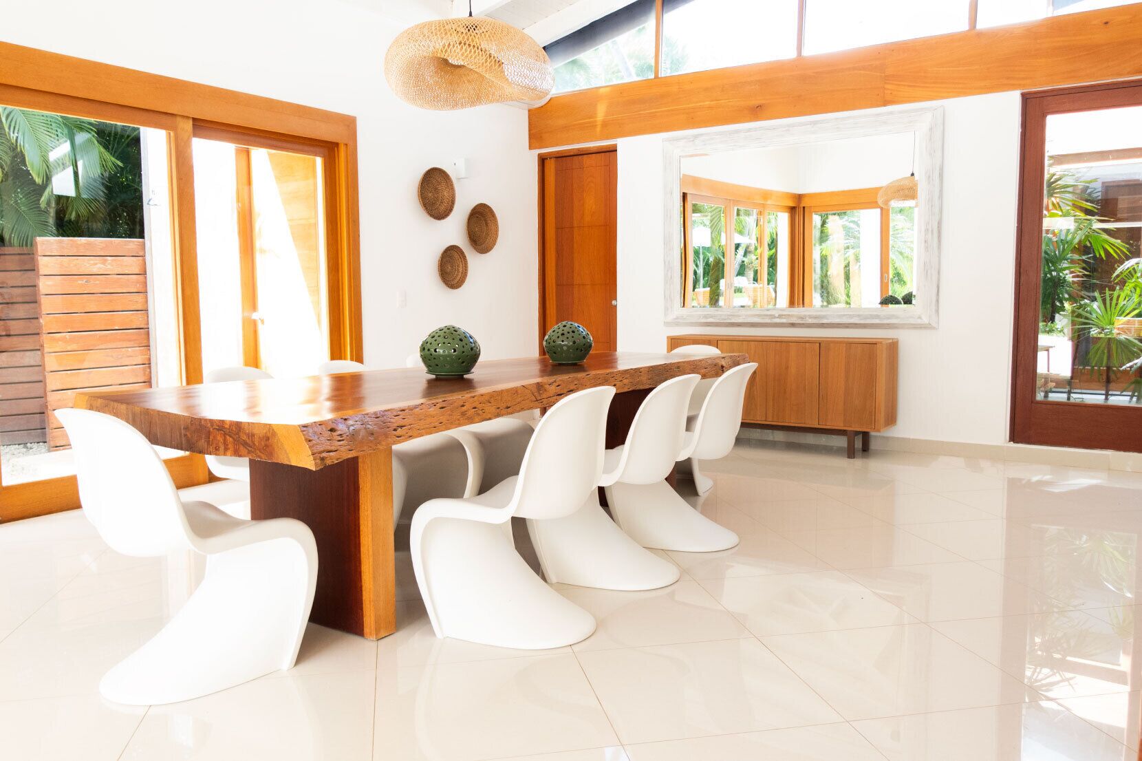 Un comedor moderno con una mesa de madera, sillas blancas y un amplio ventanal con vista a la vegetación.