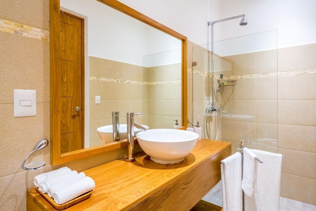 Een moderne badkamer met een houten wastafelmeubel, een grote spiegel, een witte wasbak en een douche met glazen wanden.