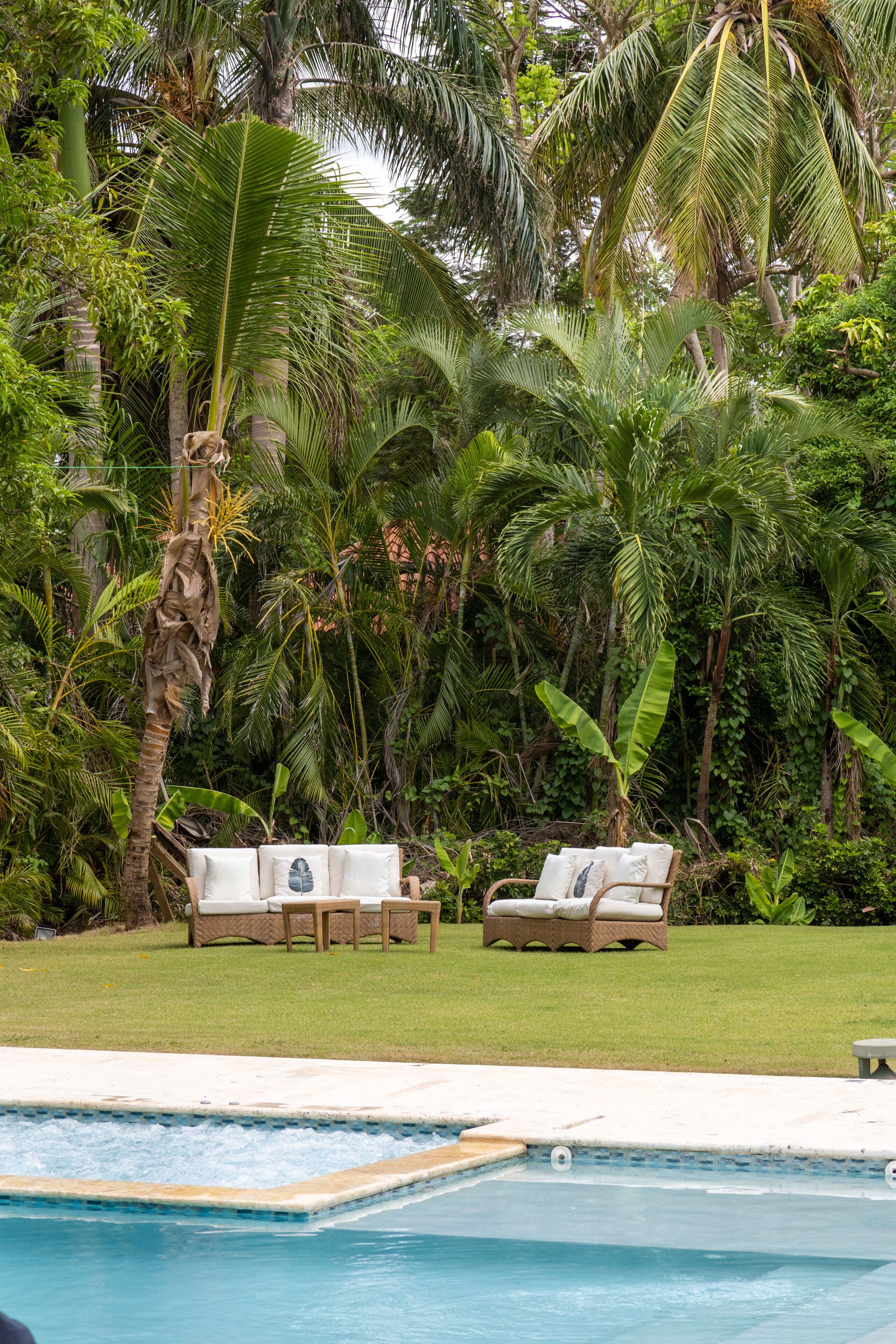 A poolside area with lounge chairs and a small table, surrounded by lush tropical vegetation.