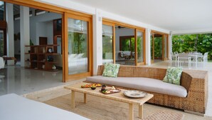 A modern living room with a wicker sofa, a wooden coffee table with snacks, and a glass door leading to a dining area.