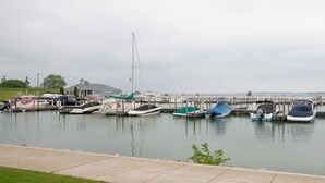 A marina with various boats docked, a grassy area in the foreground, and a building in the background. - Spectacular Waterfront Condo Retreat For 6 w/ Cedar Point View! (Sandusky)