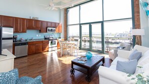 A spacious living room with a large window, a kitchen with wooden cabinets, and a dining area. - Spectacular Waterfront Condo Retreat For 6 w/ Cedar Point View! (Sandusky)