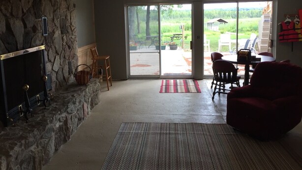 Een ruime woonkamer met een stenen open haard, een grote schuifpui naar een terras buiten, en een rode fauteuil.