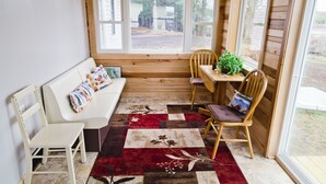 Een gezellige kamer met een houten bankje, een kleine tafel met een plant en uitzicht op het landschap door grote ramen.