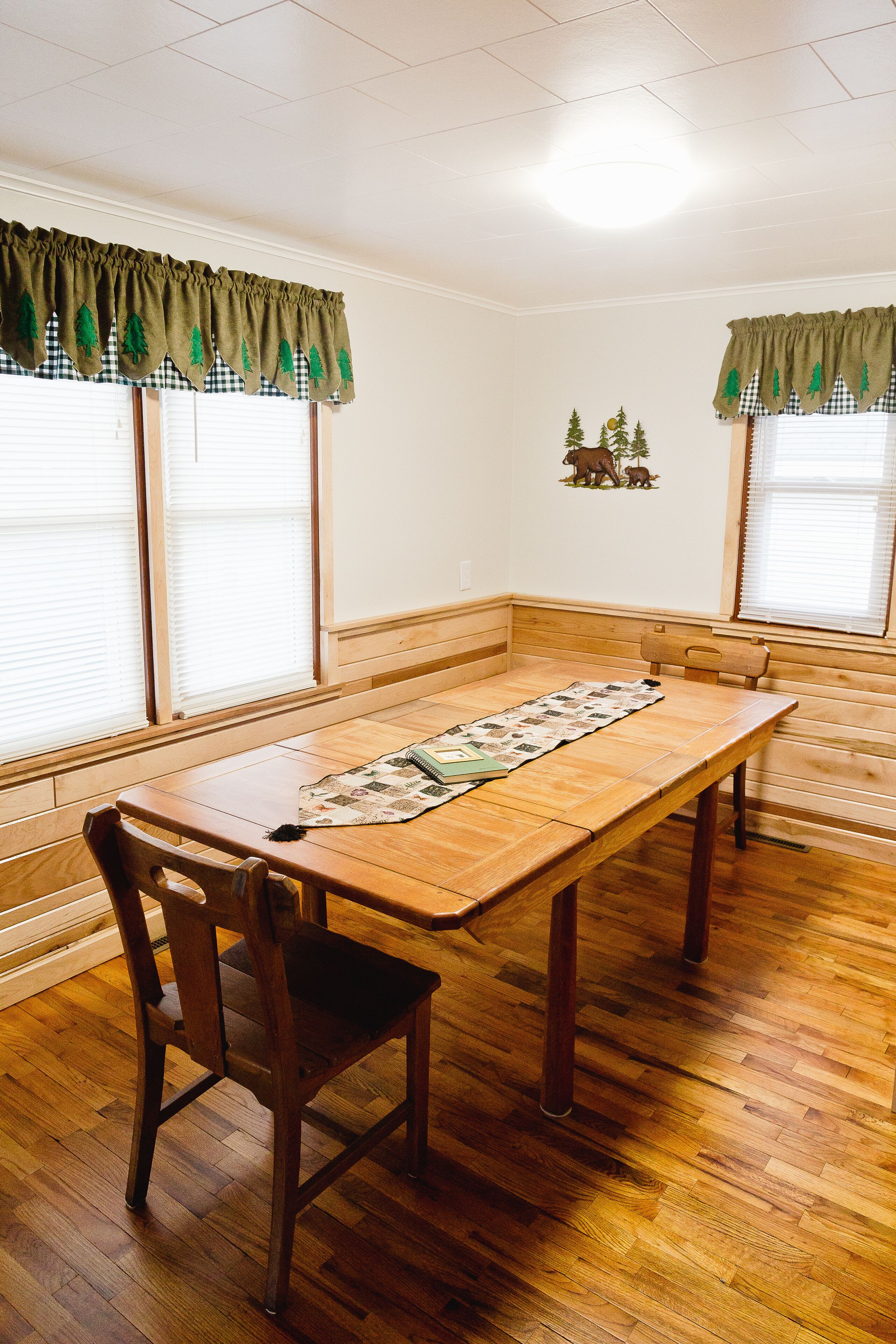 A dining area with a wooden table, chairs, and a checkered window valance.