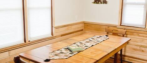 A dining area with a wooden table, chairs, and a checkered window valance.