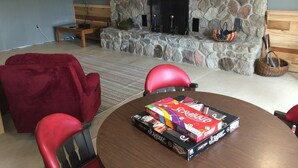 Een gezellige zithoek met een stenen openhaard, rode stoelen en een Scrabble speldoos op een tafel.
