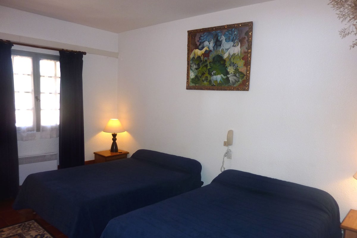 A hotel room with two beds, a lamp, a painting on the wall, and a telephone.