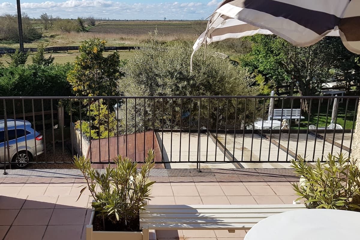 A balcony with a view of a train, a parked car, and a grassy field.