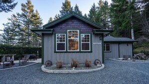 A small, single-story building with a dark roof and light walls, labeled "PRIVATE RENTAL." It features a gravel driveway and is surrounded by trees. - Cozy Cabin Getaway. Fireplace, king bed, hot tub, Pet OK. (Victoria)