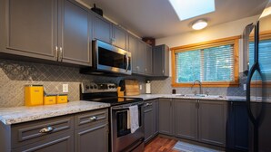 A modern kitchen with grey cabinets, a stainless steel refrigerator, a microwave, and a built-in oven. - Cozy Cabin Getaway. Fireplace, king bed, hot tub, Pet OK. (Victoria)