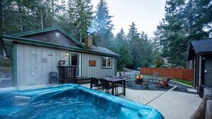 A backyard with a hot tub, outdoor seating, and a barbecue grill. - Cozy Cabin Getaway. Fireplace, king bed, hot tub, Pet OK. (Victoria)