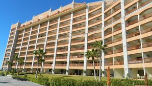A multi-story hotel with balconies, a parking area, and palm trees. - Beach Front Convenience..Steps to the Beach and Pool !  (Puerto penasco)