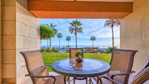 A round table with four chairs, a potted plant, and a view of palm trees and a pool. - Beach Front Convenience..Steps to the Beach and Pool !  (Puerto penasco)