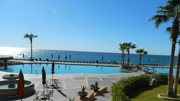 A resort pool area with a view of the ocean, lounge chairs, and palm trees. - Beach Front Convenience..Steps to the Beach and Pool !  (Puerto penasco)