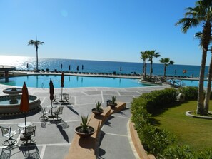 A resort pool area with a view of the ocean, lounge chairs, and palm trees. - Beach Front Convenience..Steps to the Beach and Pool !  (Puerto penasco)