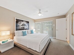 A bedroom with a bed, nightstand, ceiling fan, window blinds, and a door. - Modern, Luxurious Home in Park Shore w/Private Beach Access & Heated Pool (Naples)