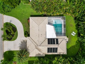 Vista aérea de una casa moderna con piscina, rodeada de exuberante vegetación y palmeras.