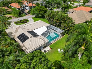 An aerial view of a house with a large glass conservatory, surrounded by lush greenery and palm trees. - Modern, Luxurious Home in Park Shore w/Private Beach Access & Heated Pool (Naples)