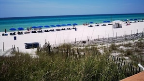Ein Strand mit Reihen blauer Sonnenschirme und Liegestühle, feiner weißem Sand und einem klaren, blauen Meer.