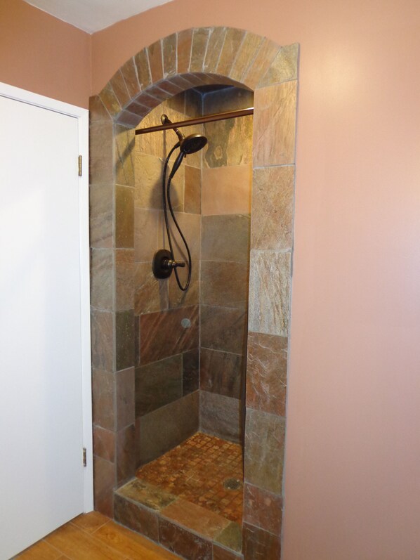 A shower with a stone arch design, a handheld showerhead, and a wall-mounted control.
