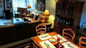 A cozy living room with a sofa, a dining table set with placemats, and a wooden cabinet with glass doors. - 3BR Townhouse - Your Home Away from Home (mammoth lakes)