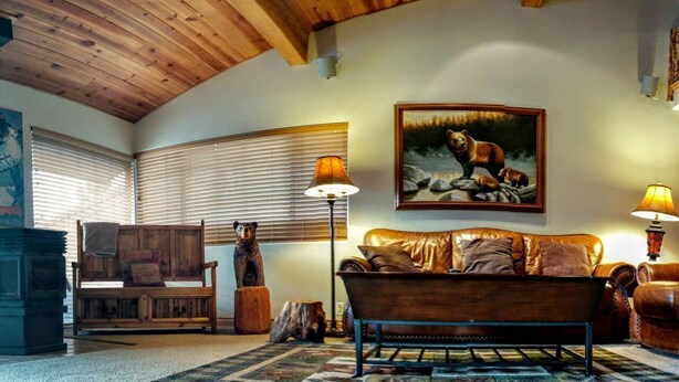 A cozy living room with a wooden ceiling, a large painting of a bear, a leather sofa, and two lamps. - 3BR Townhouse - Your Home Away from Home (mammoth lakes)
