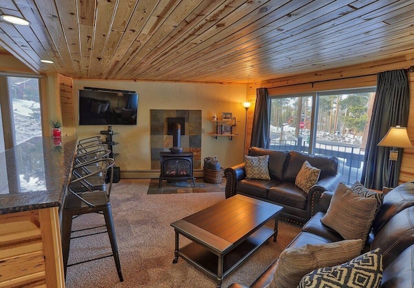 A cozy living room with a fireplace, leather sofa, and a TV mounted on the wall.