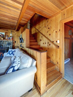 A wooden interior with a staircase, a stone fireplace, and a sofa with patterned cushions. - The Haystack House-Cannon Beach Oceanfront Home Steps to Haystack Rock & Midtown (Cannon Beach)