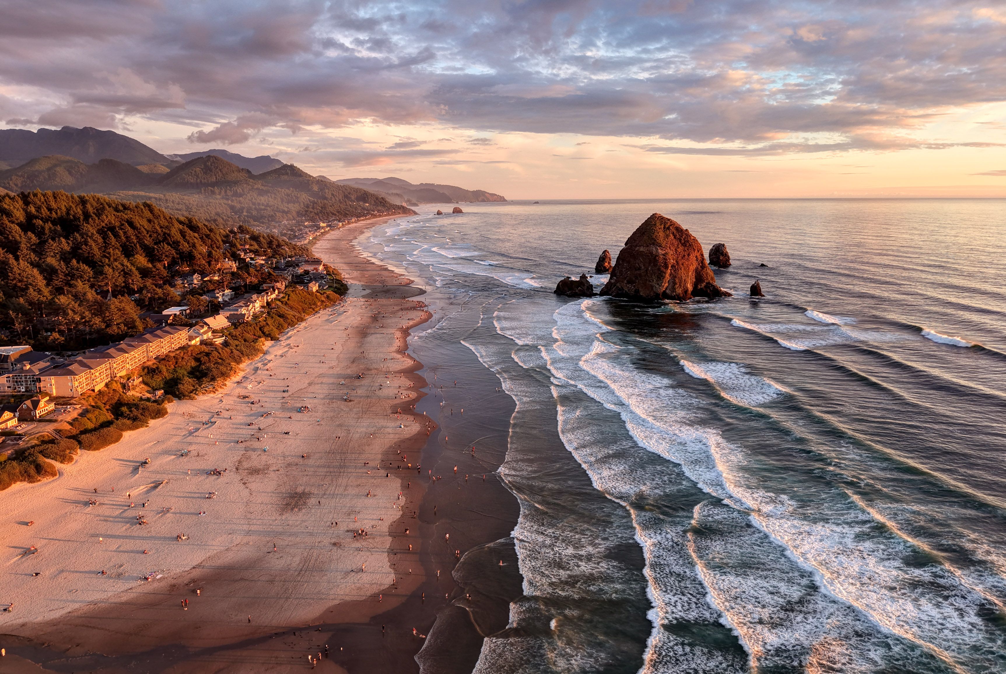 Una playa costera con un afloramiento rocoso, olas y una cadena montañosa distante.