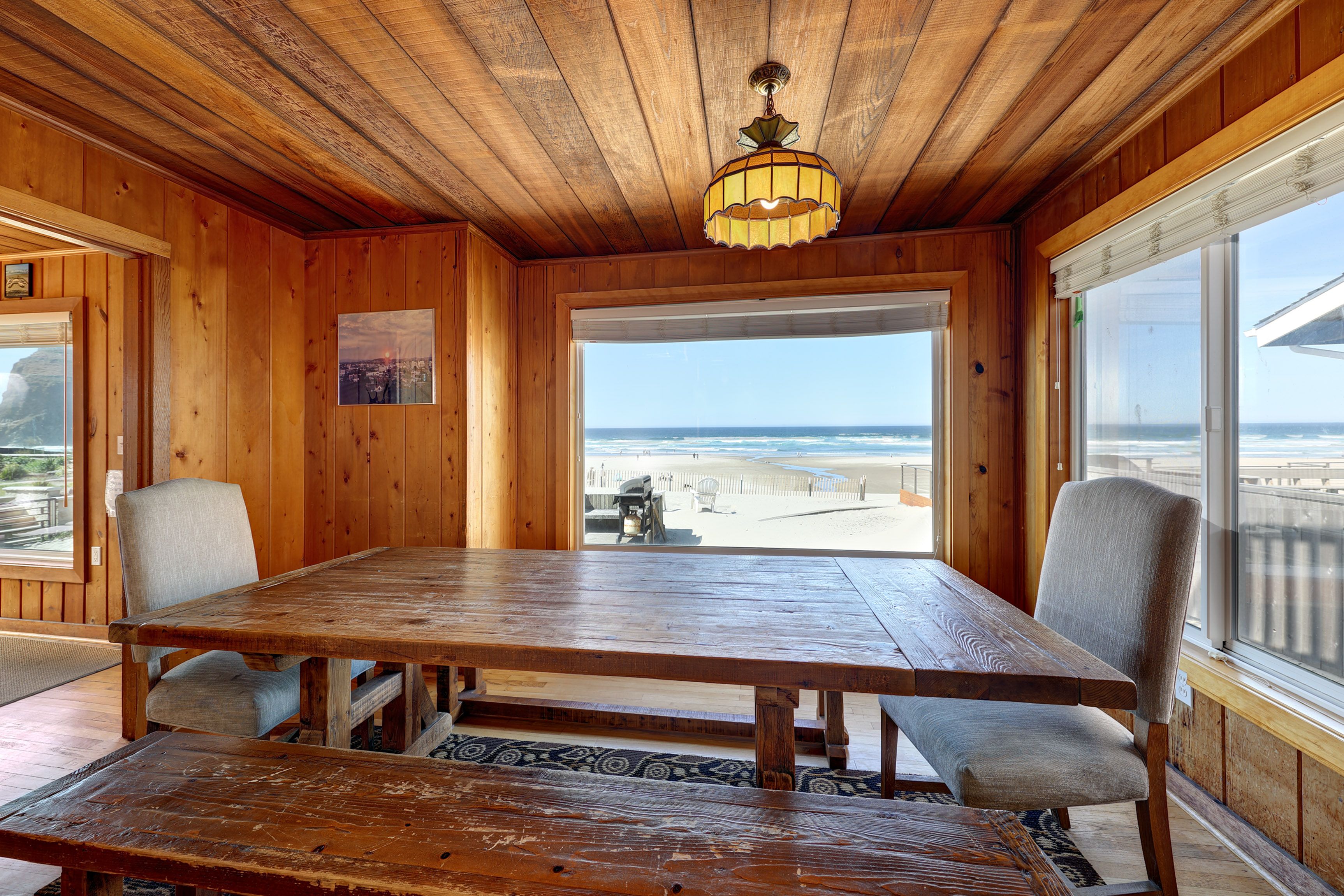 Un intérieur en bois avec une grande table, des chaises et une vue sur la plage.
