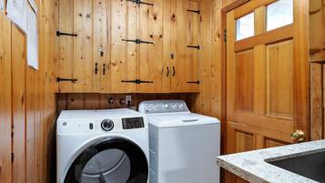 Une buanderie équipée d’armoires en bois, d’un lave-linge, d’un sèche-linge et d’un évier.