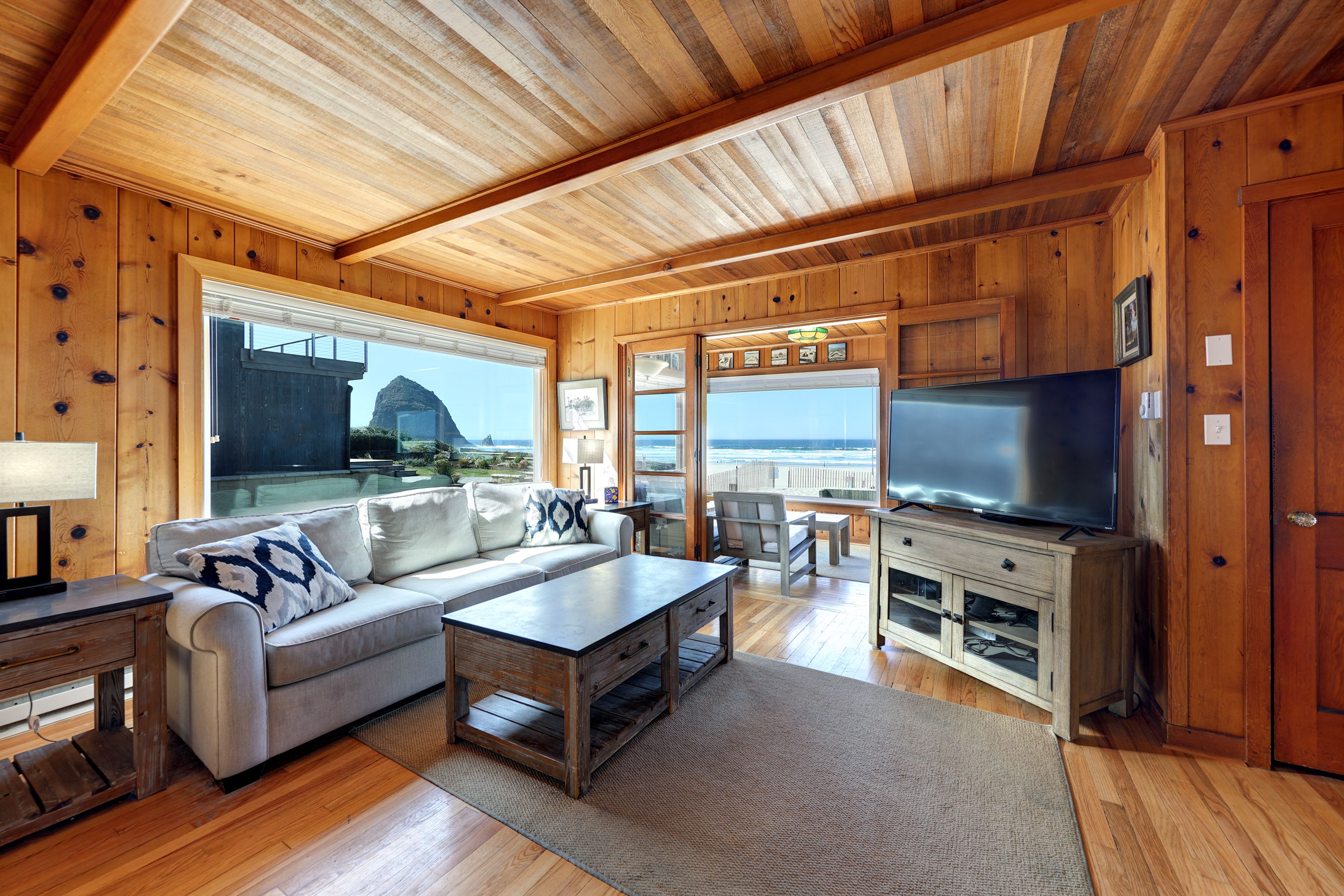 A wooden cabin interior with a sofa, coffee table, TV, and a view of the ocean.