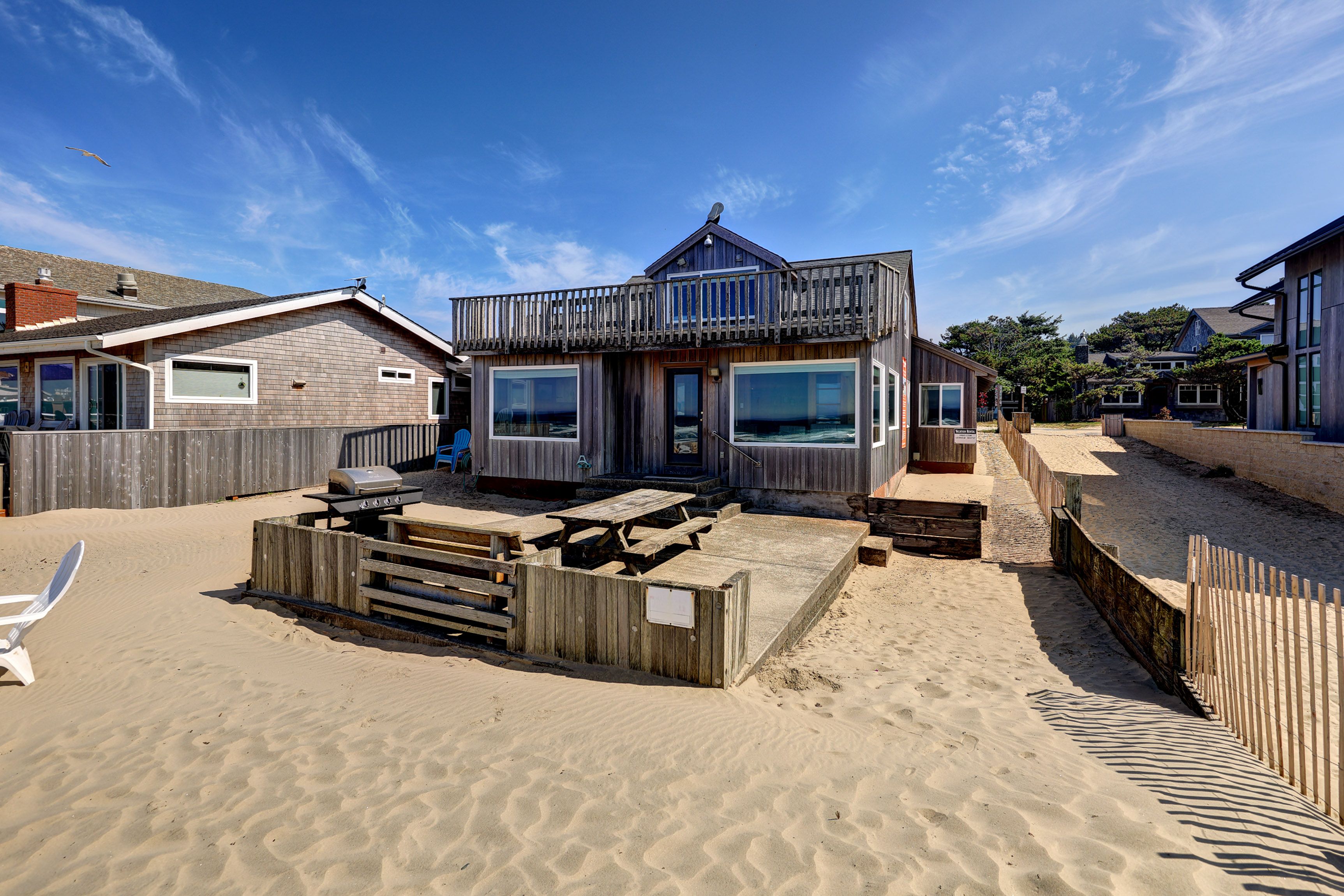 Une propriété située en bord de mer, dotée d’une terrasse en bois, d’un barbecue et offrant une vue sur l’océan.