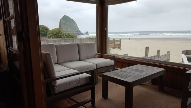 A room with a sofa and a table, a view of the beach and a rock formation. - The Haystack House-Cannon Beach Oceanfront Home Steps to Haystack Rock & Midtown (Cannon Beach)