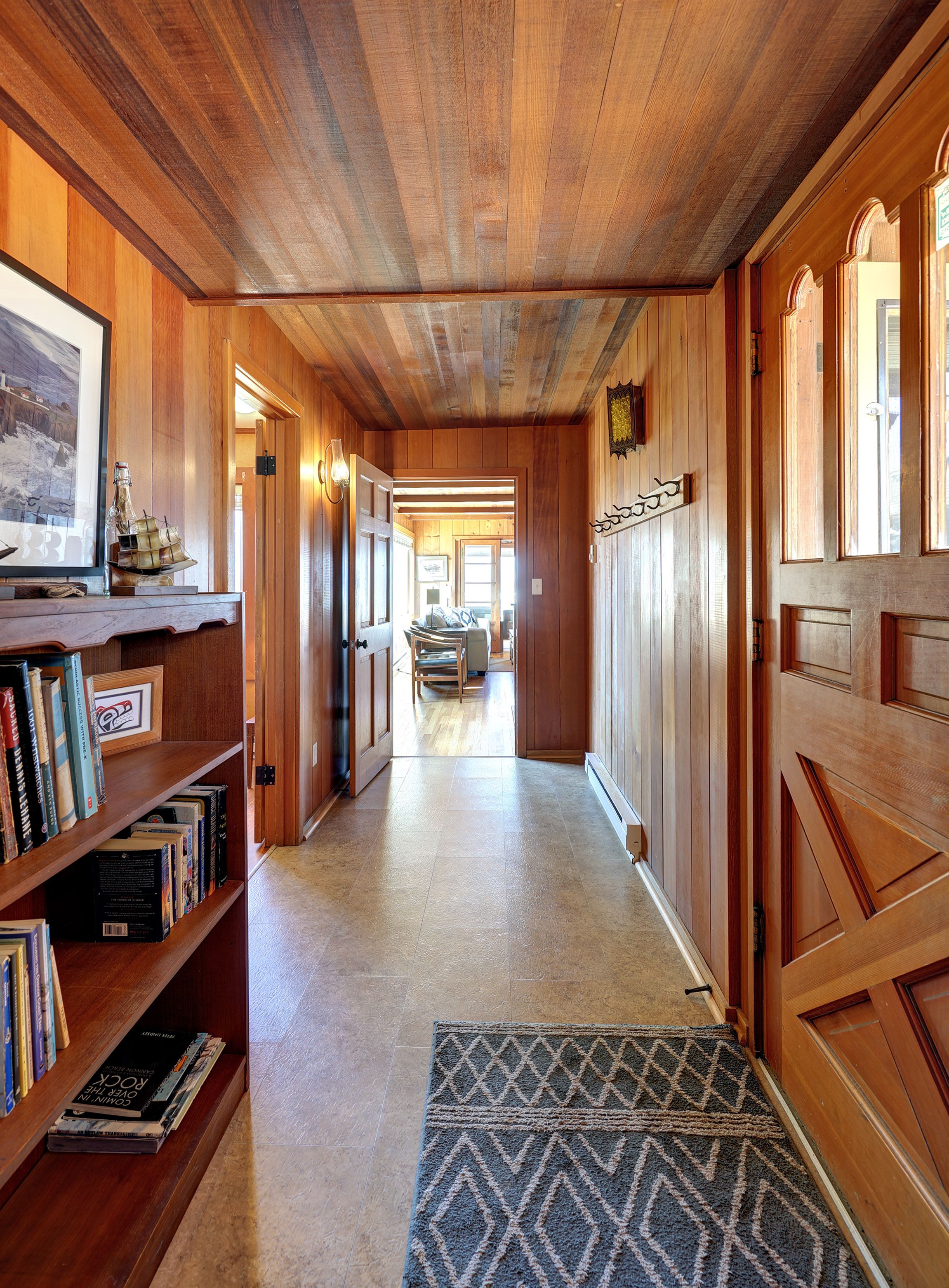Un couloir en bois, avec des étagères à livres, un tapis et une porte donnant sur une autre pièce.