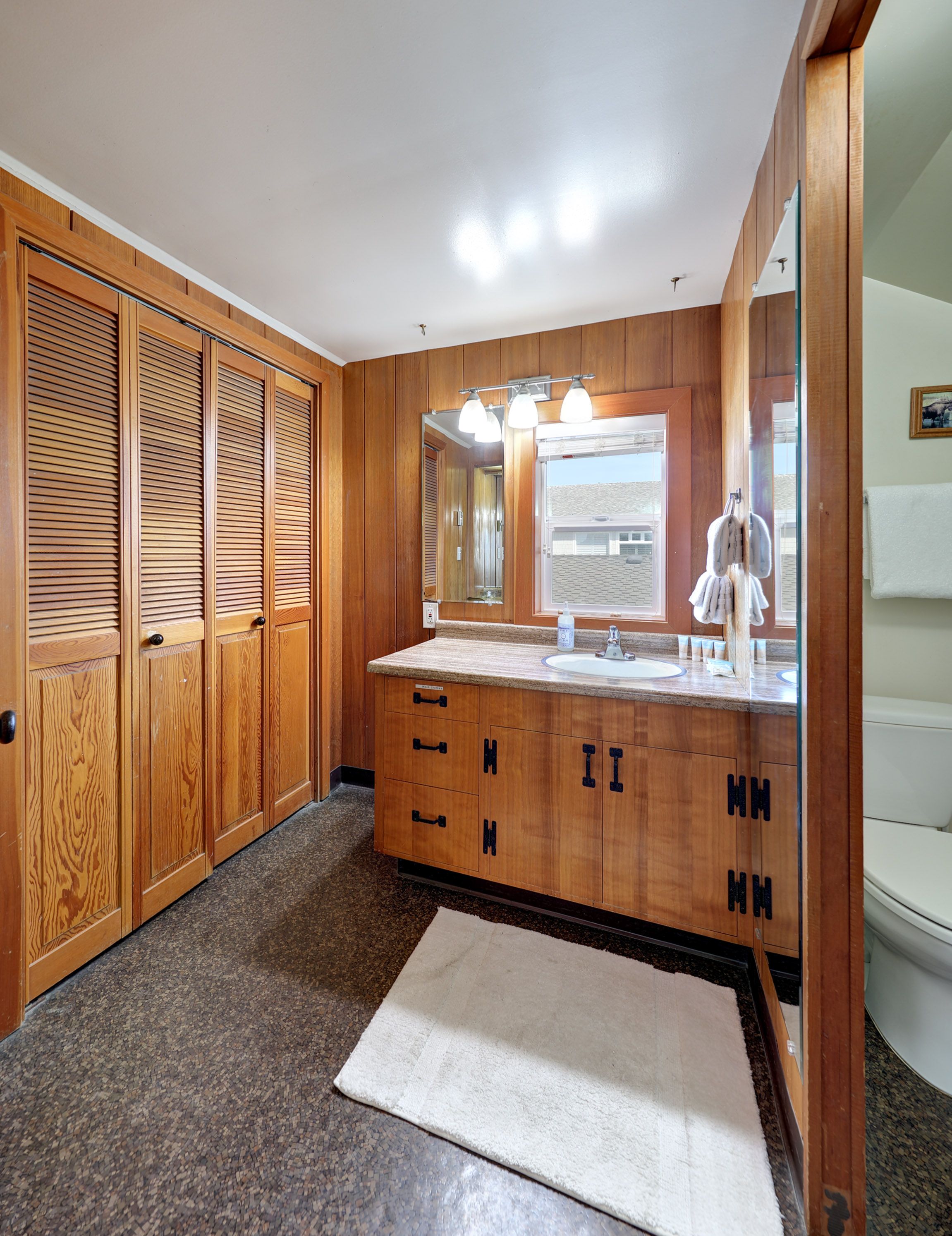 Un baño con muebles de madera, un lavamanos, un espejo y una ventana.