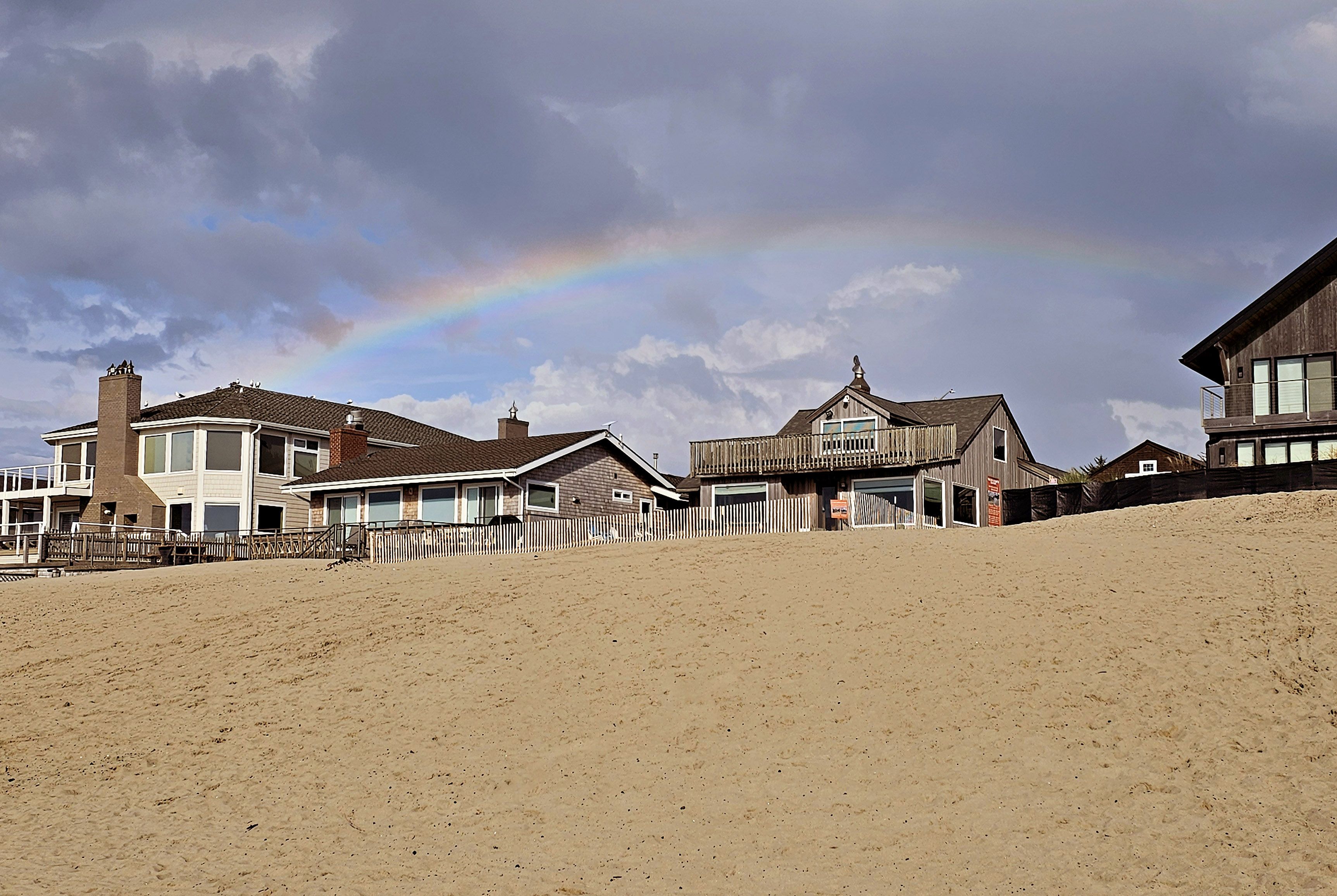 Une propriété située en bord de mer, comprenant plusieurs maisons, une clôture en bois et un arc-en-ciel bien visible.