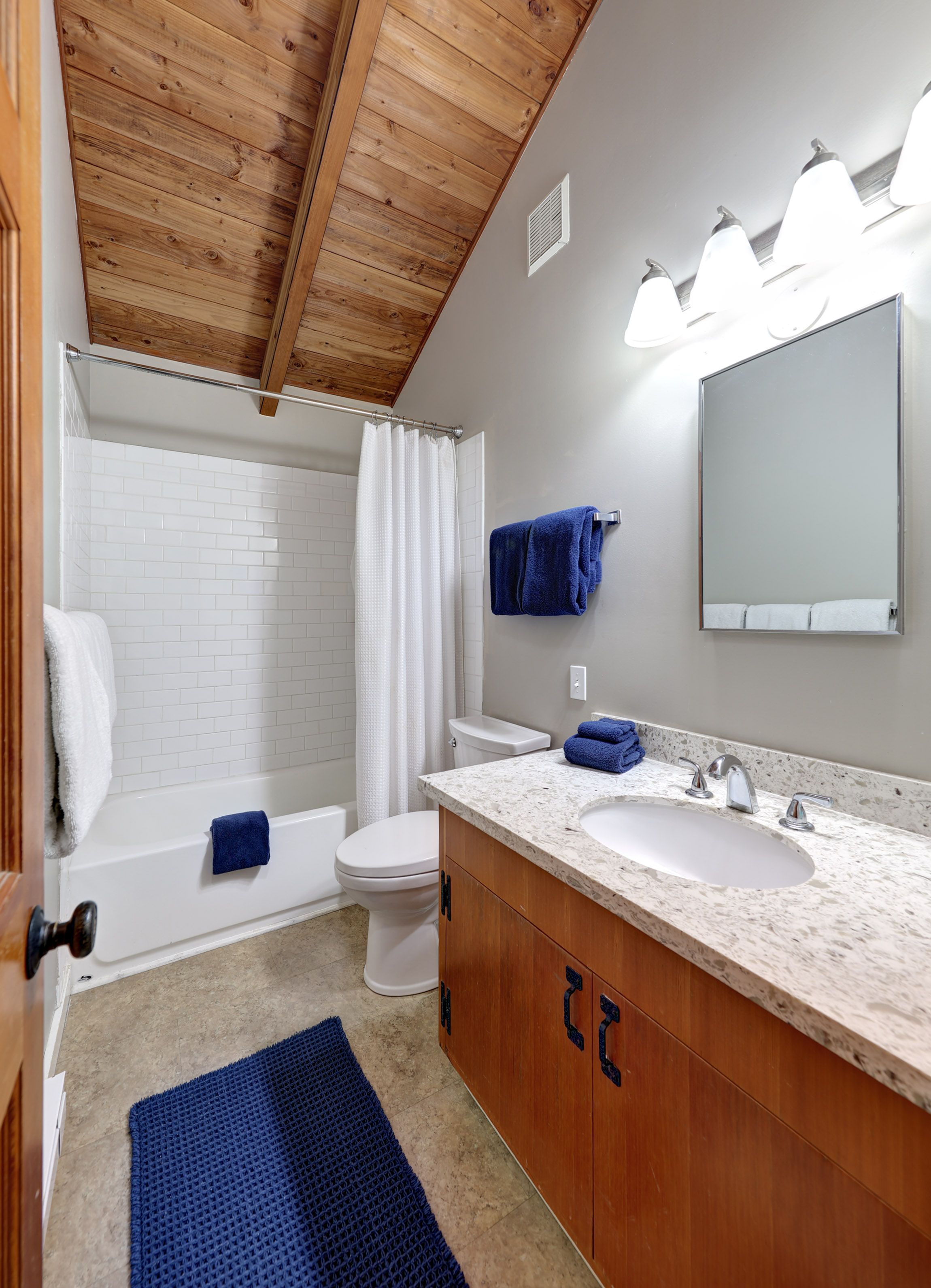 A bathroom with a bathtub, toilet, and sink, wooden ceiling, and a large mirror.