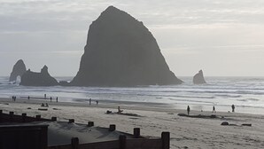A beach with large rock formations in the distance and people walking along the shore. - The Haystack House-Cannon Beach Oceanfront Home Steps to Haystack Rock & Midtown (Cannon Beach)