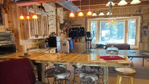 A rustic wooden interior with a bar area, stools, and a view of the outdoors through large windows.