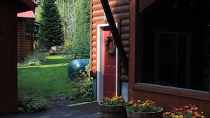 A log cabin with a red door, wooden barrels with flowers, and a green lawn.