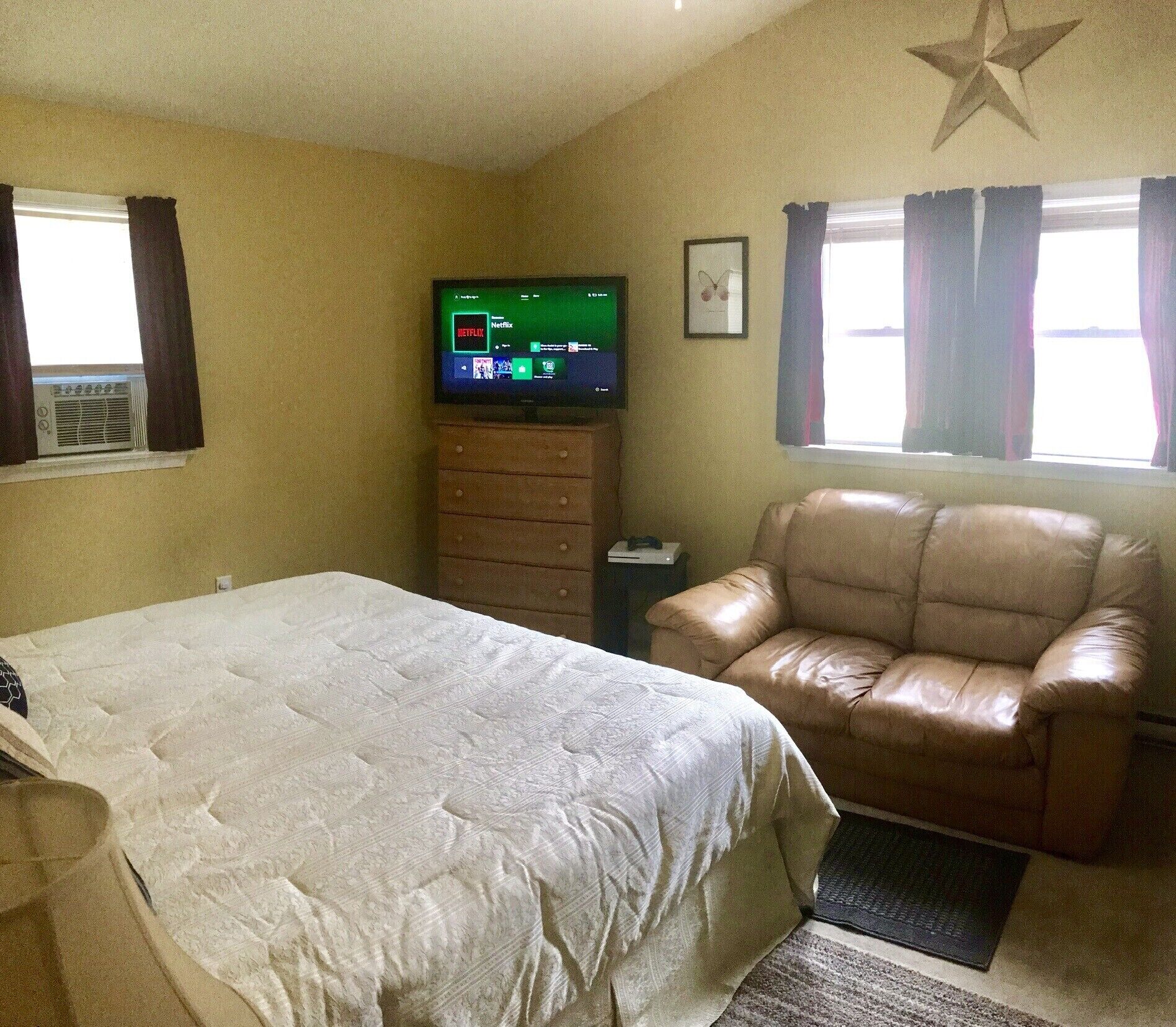Een kamer met een bed, een leren fauteuil, een televisie waarop Netflix wordt weergegeven en een sterren decoratie aan het plafond.