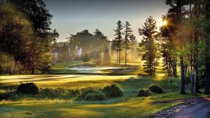 Een golfbaan met een huis op de achtergrond, omringd door bomen en een heldere lucht.