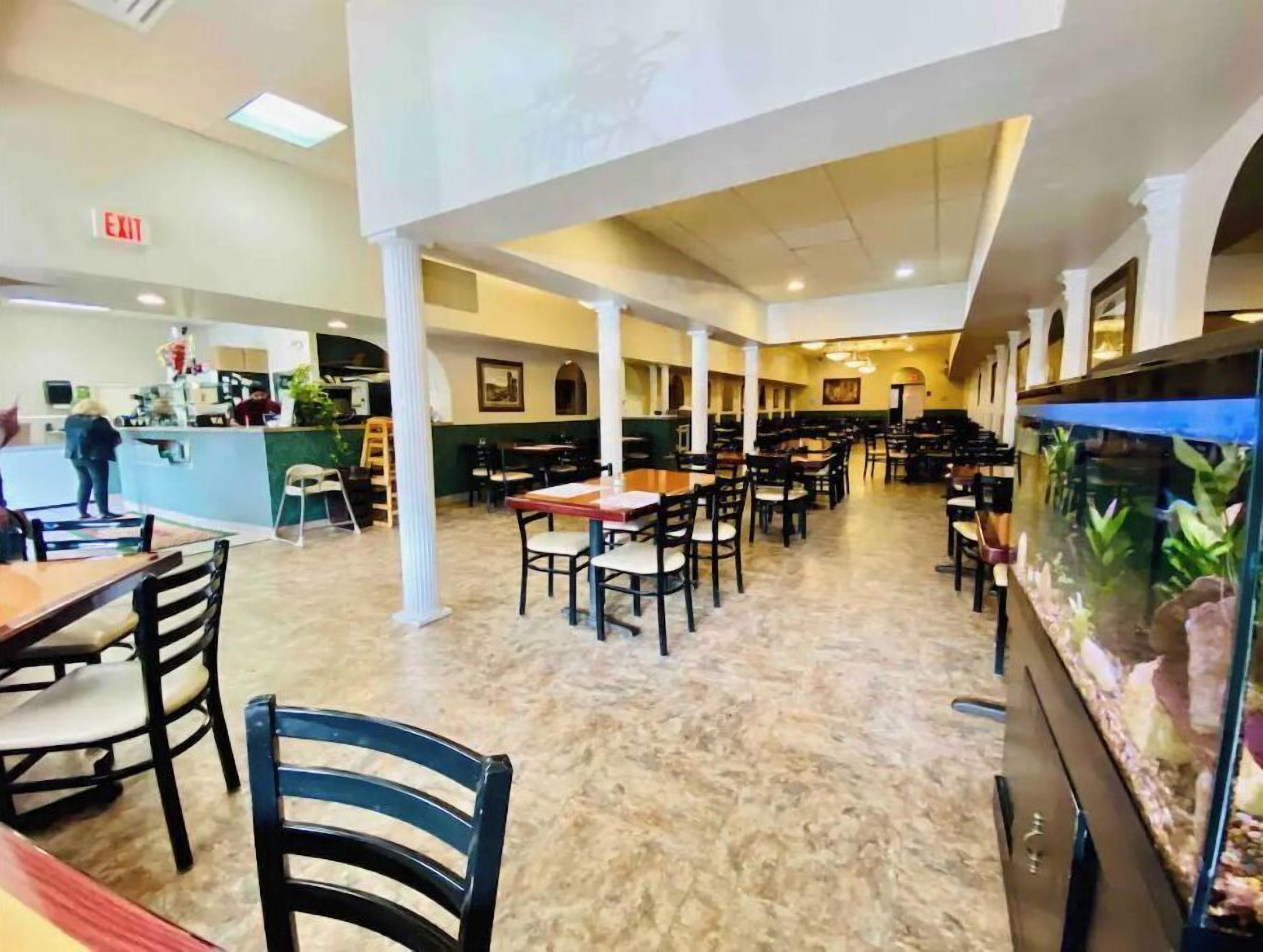 A spacious restaurant with high ceilings, multiple tables and chairs, a counter area, and a large fish tank.